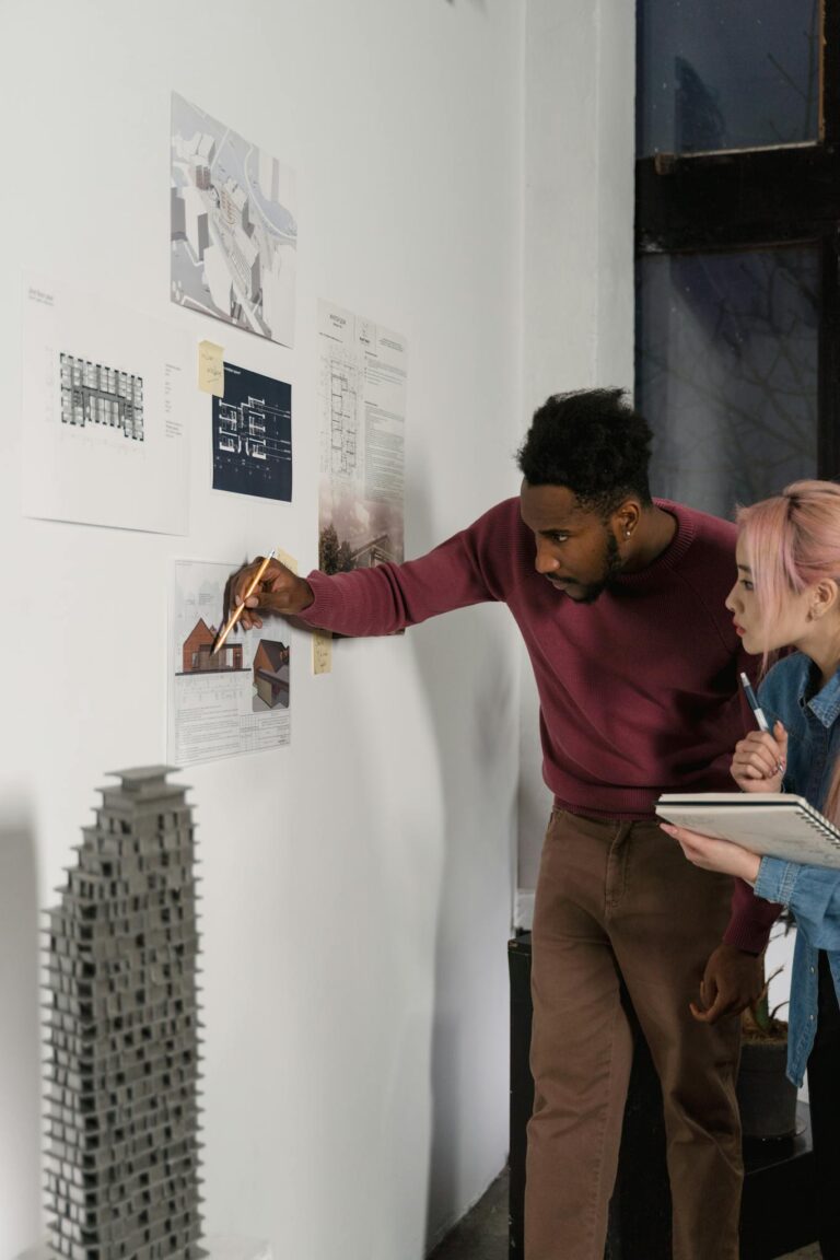 Two professionals discussing architectural designs on a white wall in a modern office setting.